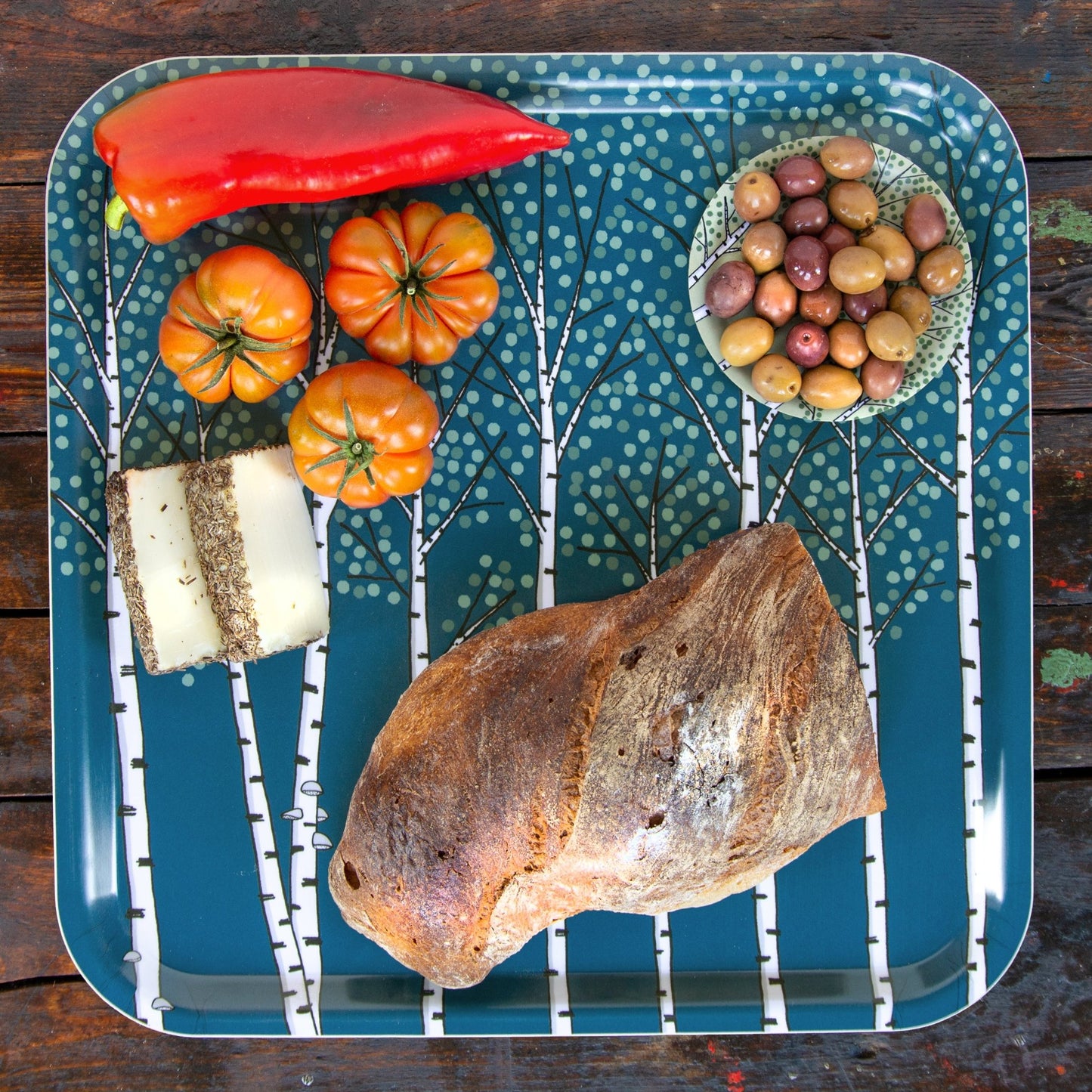Skandinavisches Frühstückstablett aus Holz mit Birken-Motiv in Dunkelblau. Großes, quadratisches Serviertablett, dekoriert mit frischem Brot, Oliven, Tomaten, Käse und Paprika. Nachhaltiges Design-Objekt für Küche und Reisen.