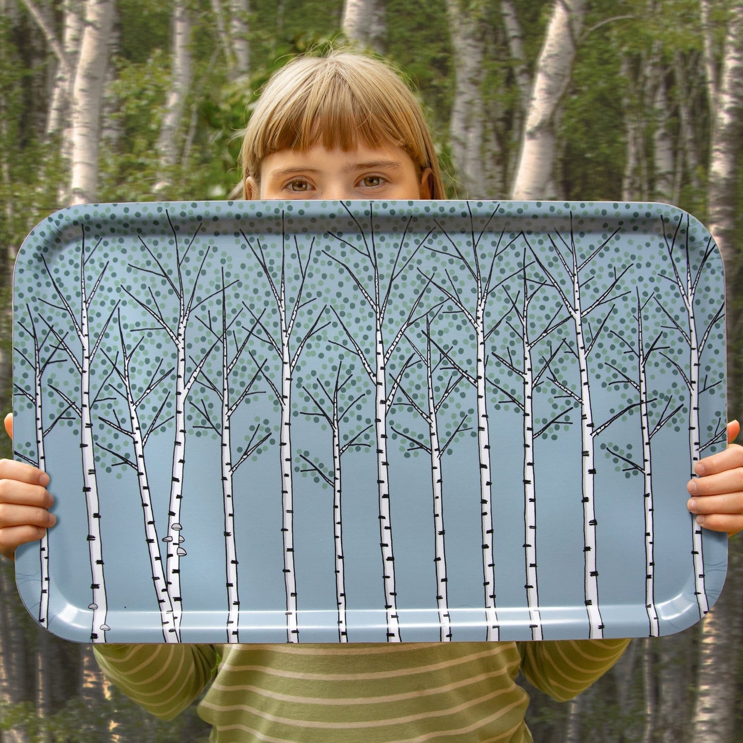 Mädchen hält ein großes skandinavisches Holztablett mit Pflanzen-Motiv in einem Birkenwald. Authentisches Natur-Design Produktfoto unseres deutsch-schwedischen Labels, das skandinavische Gemütlichkeit zeigt.