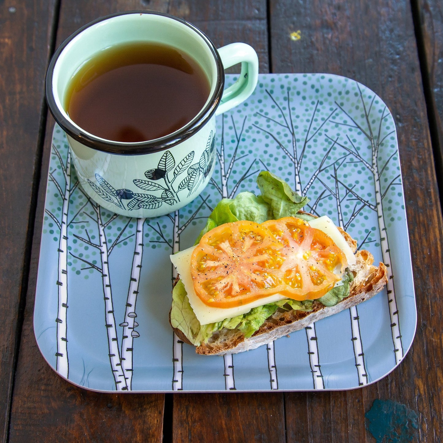 Skandinavischer Frühstücksteller aus Holz mit Birken-Motiv in Hellblau. Kleines, quadratisches Serviertablett, ideal genutzt als kleiner Teller mit einer Kaffeetasse und einem belegten Käsebrot.