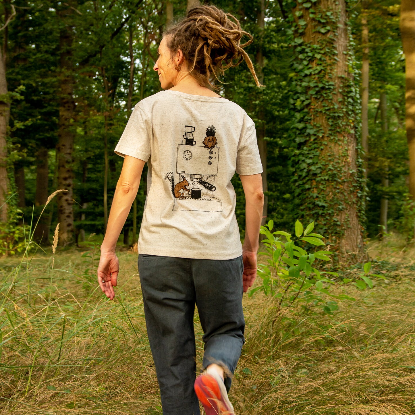 Kaffee T-Shirt für Damen mit detailreichem Backprint, getragen von einer Frau, die im Wald steht und geht. Auf dem Motiv bedienen ein Eichhörnchen und ein Hörnchen eine Espressomaschine.
