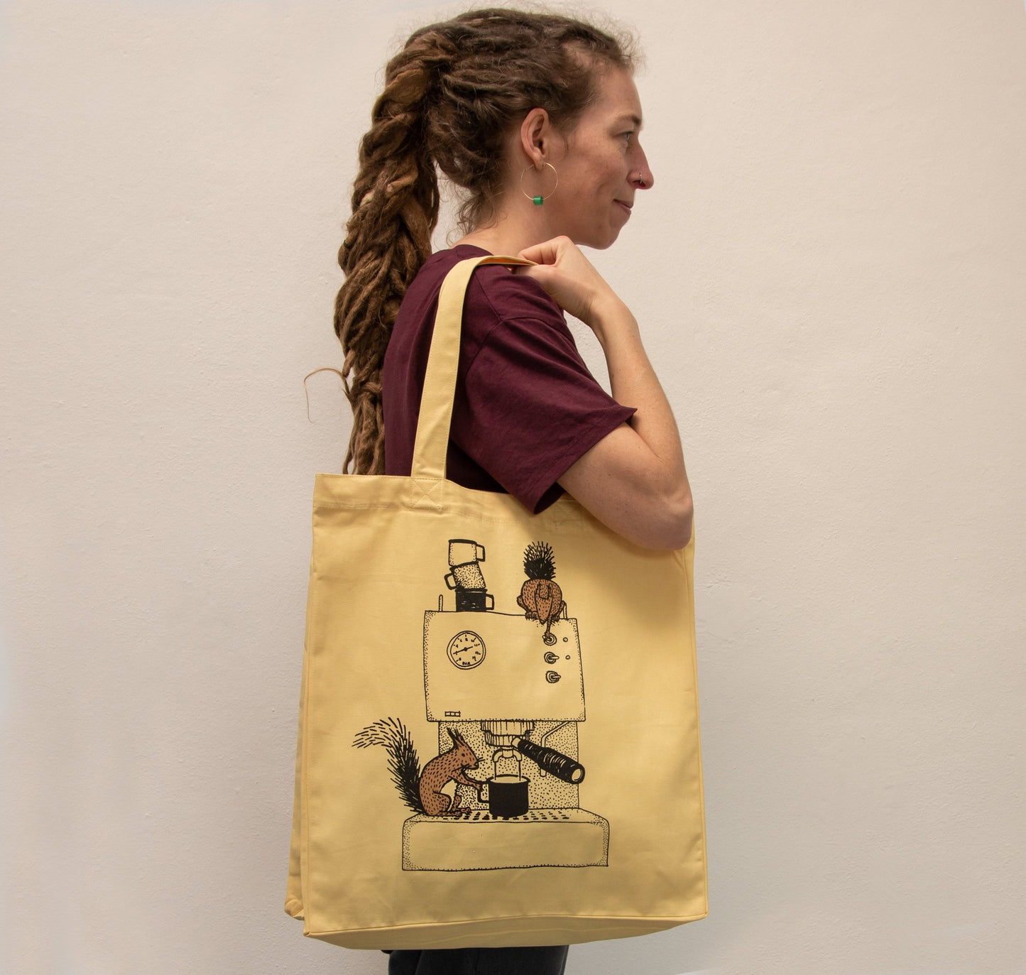 Kaffee Jutebeutel in Gelb getragen von einer Frau. Der farbenfrohe Shopper mit Eichhörnchen-Motiv zeigt sich als praktischer Alltagsbegleiter und kreatives Geschenk für Frauen.