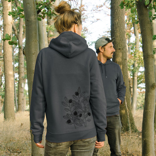 Blaubeere Pullover im Unisex-Schnitt in India Ink Gray. Eine Frau und ein Mann präsentieren gemeinsam den dunkelgrauen Partnerlook-Kapuzenpullover im Wald von vorne und hinten.
