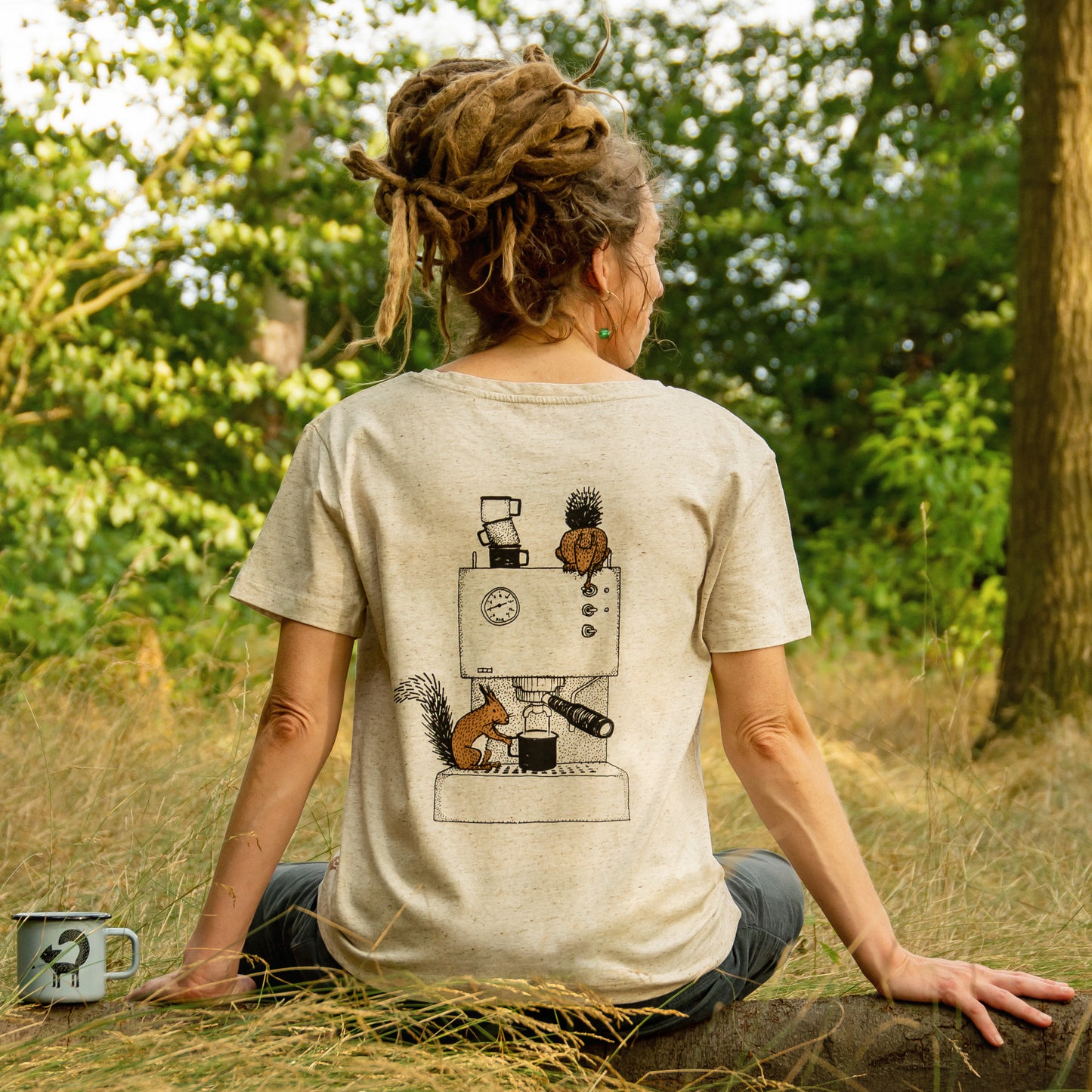 Kaffee T-Shirt mit Backprint für Damen, getragen von einer Frau im Wald. Das detailreiche Grafik-Motiv zeigt ein Eichhörnchen und ein Hörnchen, die eine Espressomaschine bedienen.