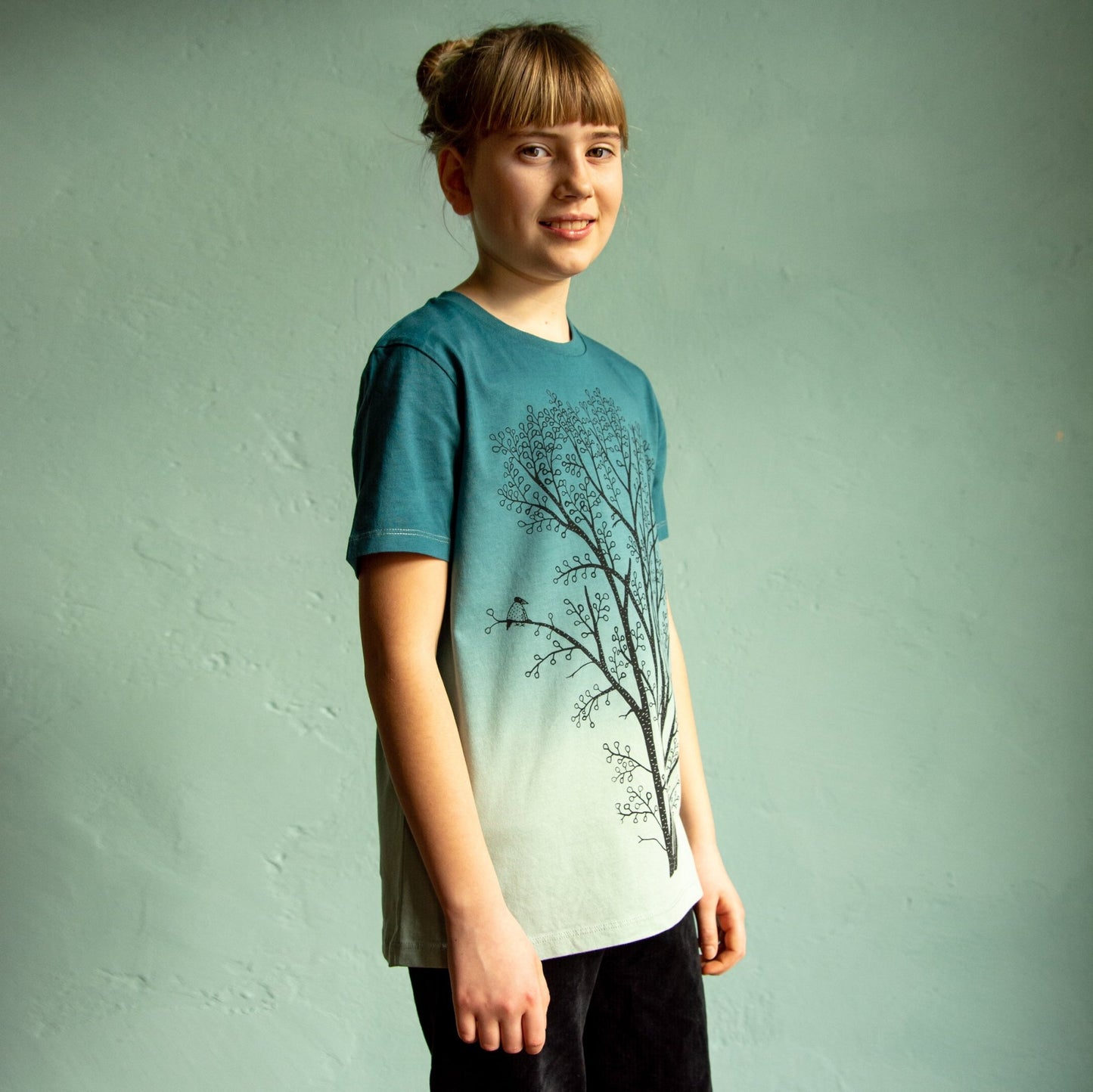 Kinder T-Shirt Baum Print als farbenfrohe Geschenkidee für Mädchen. Ein Mädchen trägt das nachhaltige Bio-Oberteil, das von Hand im eigenen Atelier in Hannover bedruckt wurde.
