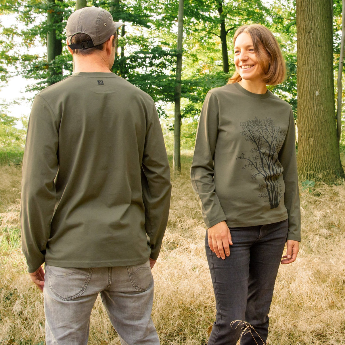 Langarmshirt Baum Kollektion aus nachhaltiger Bio-Baumwolle. Ein herbstliches Outdoor-Tragebild zeigt eine Frau und einen Mann im oliv-grünen oder khaki farbenen Unisex-Longsleeve.
