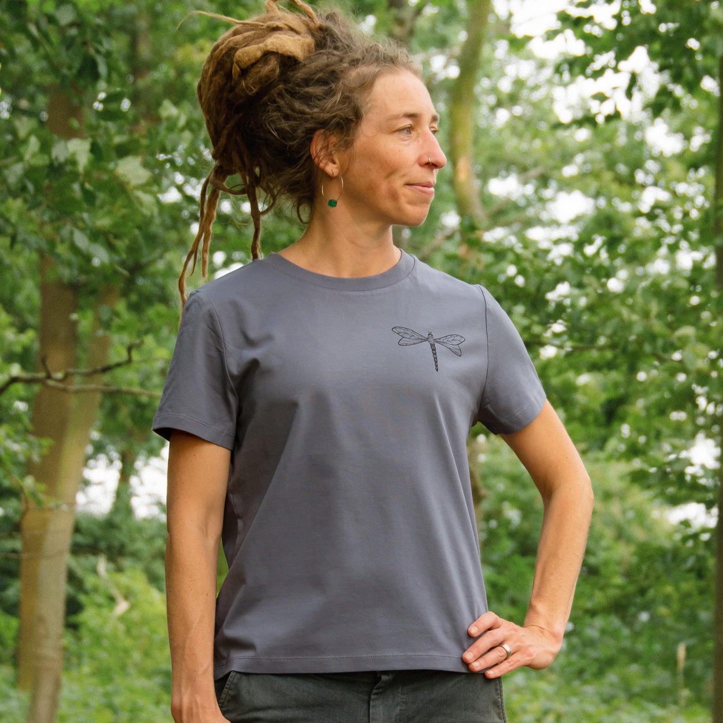 Damen Bio-T-Shirt in Blau-Grau mit kleinem Libellenmotiv auf der Brust, Model im Wald