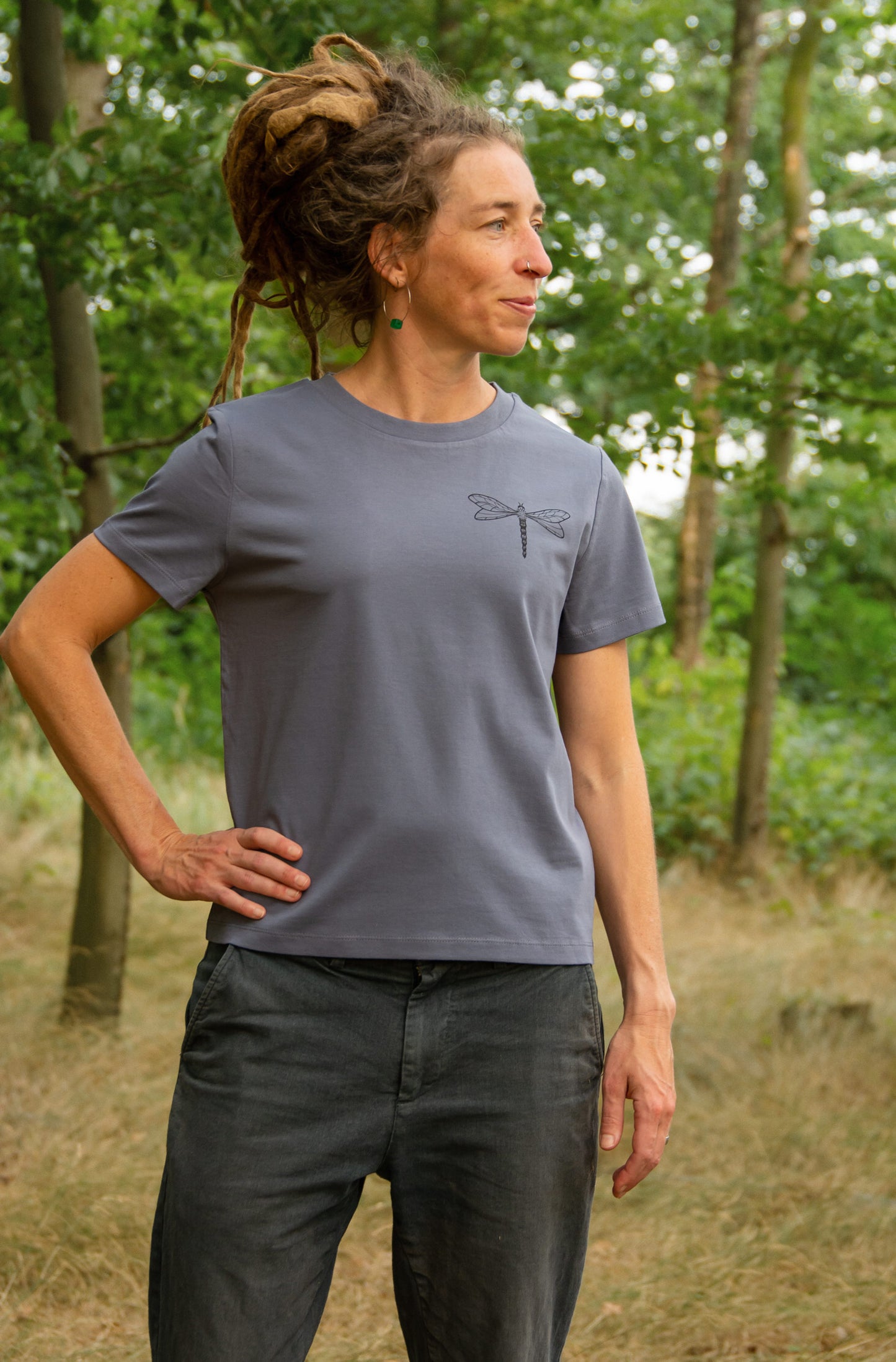 Damen Bio-T-Shirt in Blau-Grau mit kleinem Libellenmotiv auf der Brust, Model im Wald
