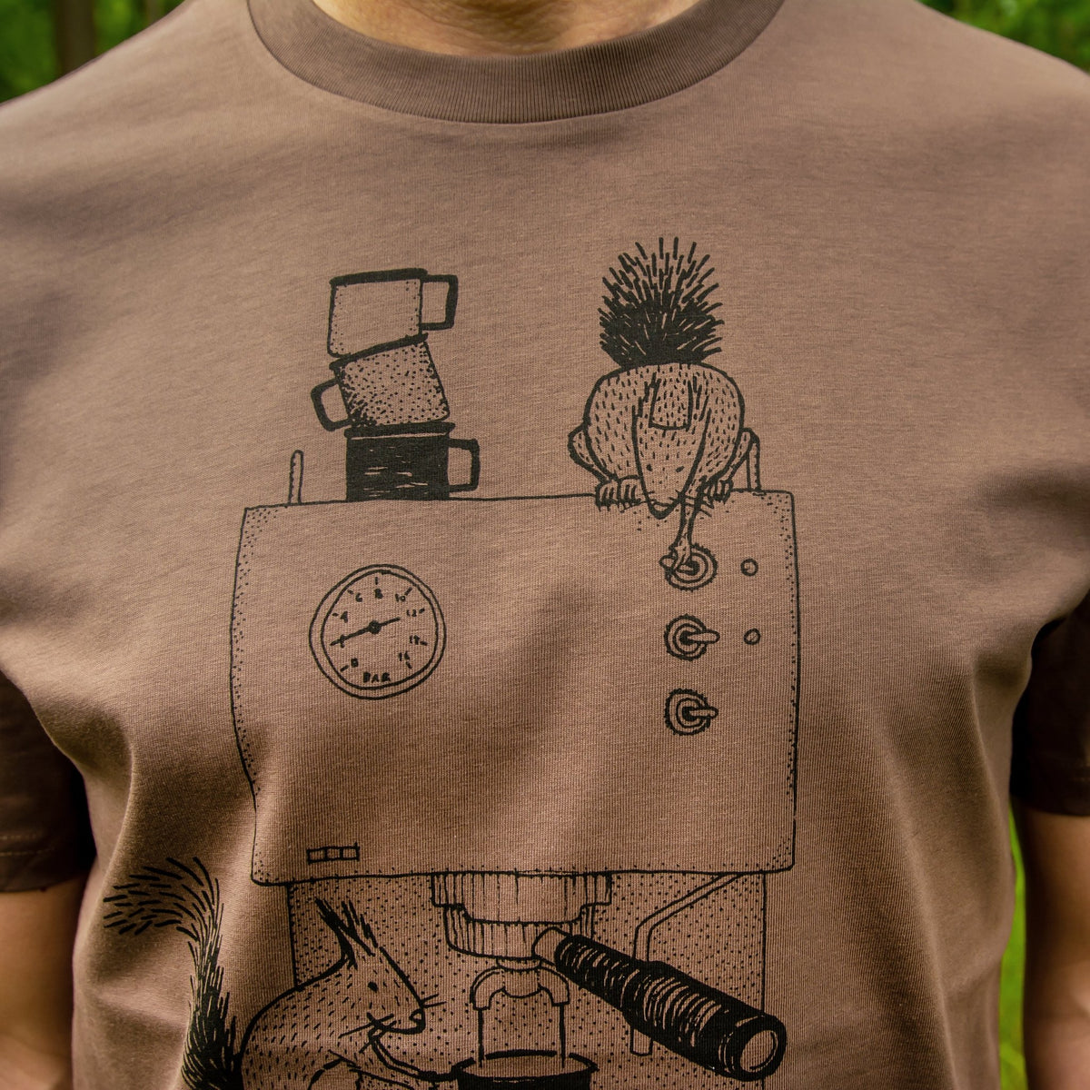Nahaufnahme der lustigen Kaffee-Illustration auf dem Herren T-Shirt in Mocca. Detailansicht des detailreichen Siebdrucks mit dem Eichhörnchen an der Espressomaschine.