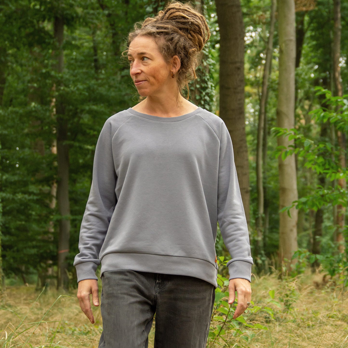 Frau steht im Wald und trägt einen grauen Bio-sweater mit Kaffee Motiv