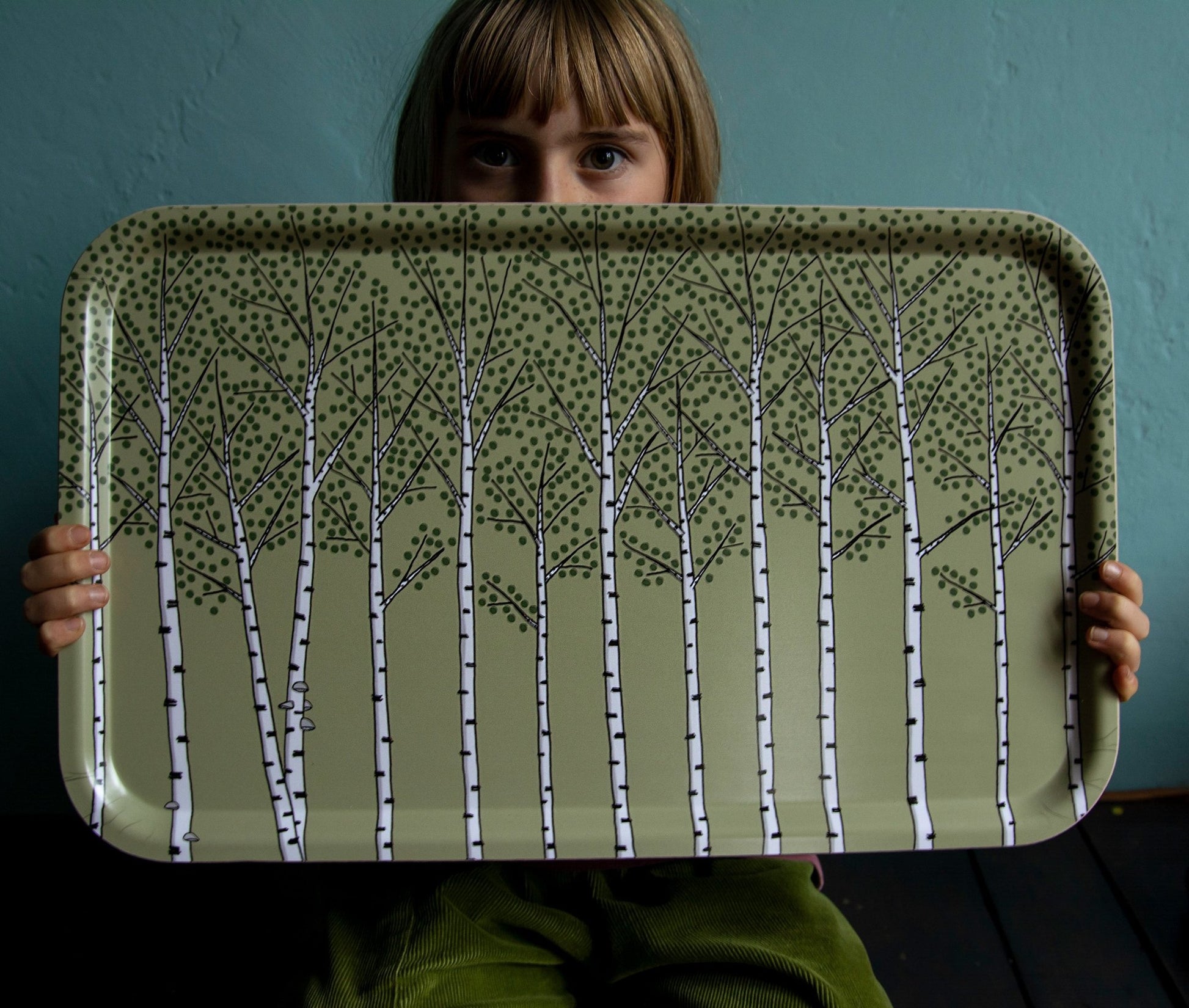 Schwedisches Design Holztablett getragen von einem Mädchen. Großes, rechteckiges Serviertablett in Grün mit kunstvollem Pflanzen-Motiv für die Küche oder das Picknick im Grünen.