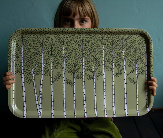 Schwedisches Design Holztablett getragen von einem Mädchen. Großes, rechteckiges Serviertablett in Grün mit kunstvollem Pflanzen-Motiv für die Küche oder das Picknick im Grünen.