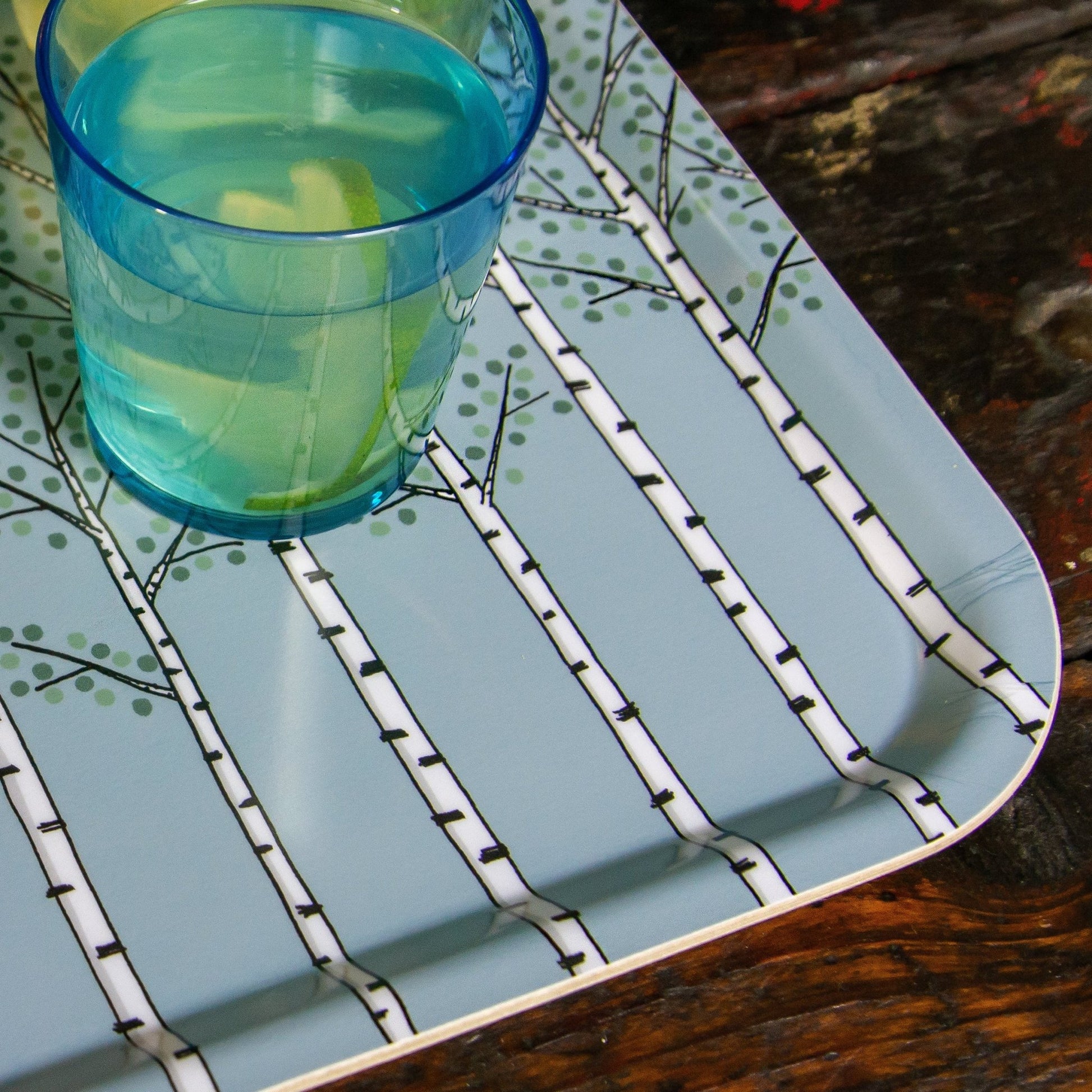 Serviertablett im Scandi-Style aus echtem Birkenfurnier in Hellblau. Detailansicht des handgefertigten Pflanzen-Motivs, serviert mit einem kühlen Glas Holunderblütensaft auf wasserunempfindlicher Beschichtung von der Insel Öland.
