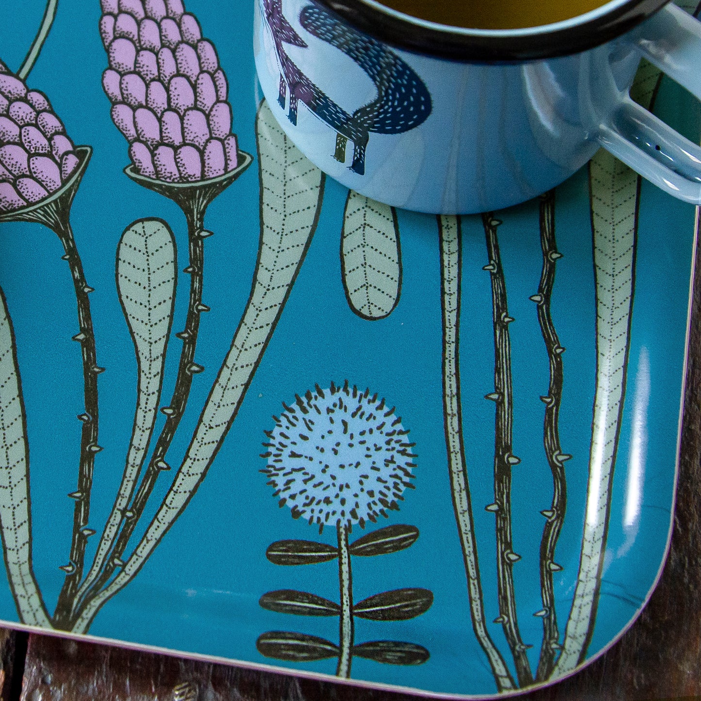 Nahaufnahme von einer botanischen Blumenwiese-Illustration mit skandinavischer Tasse. Detailansicht des kleinen dunkelblauen Serviertabletts im Scandi-Style mit unserer handillustrierten Fuchs-Emailletasse auf der schwedischen Insel Öland.