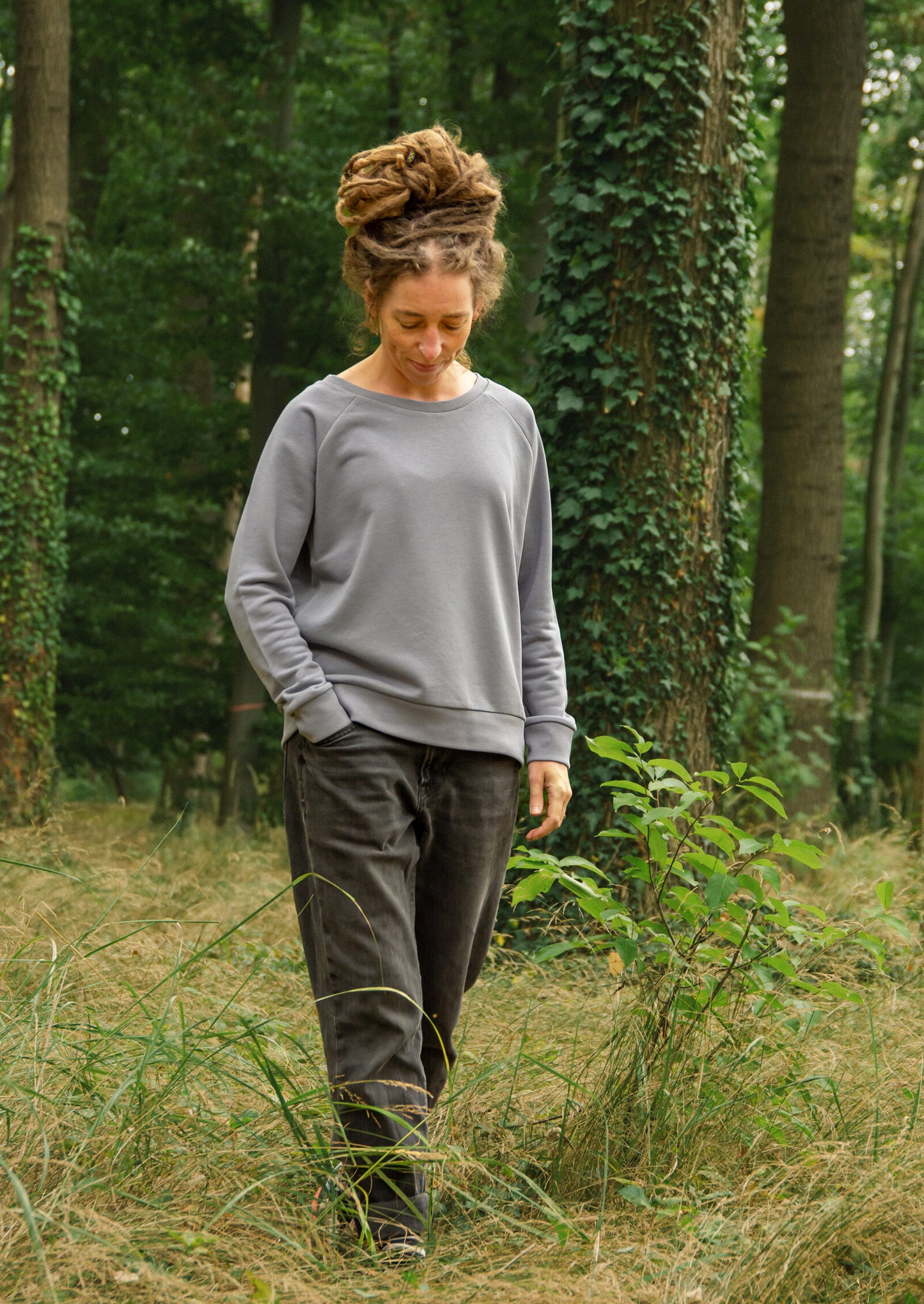 Frau spaziert im Wald mit  Bio-Pullover in lava grey und Kaffee Motiv