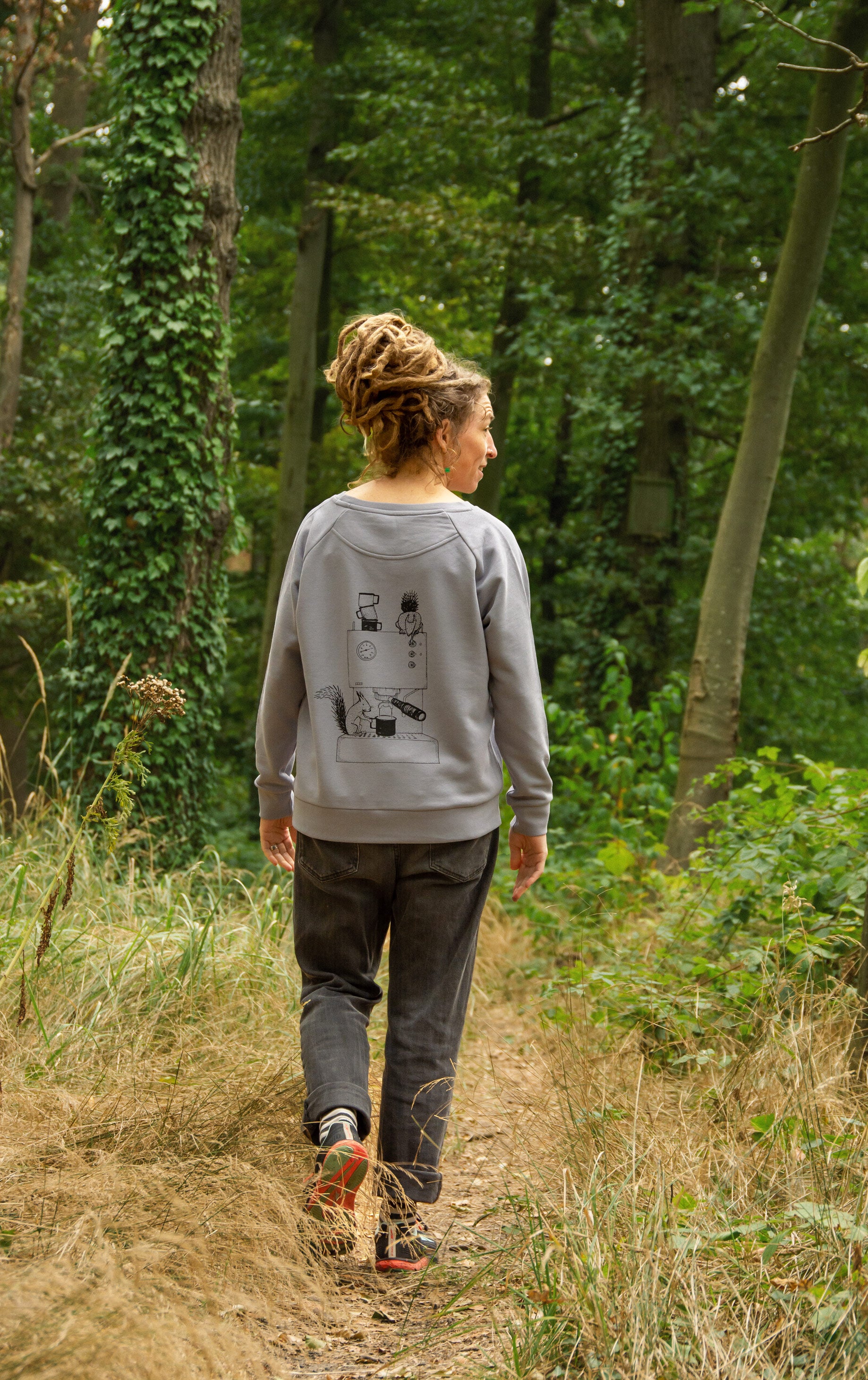 Rückansicht einer Frau im Wald mit Kaffee Pullover aus Bio-Baumwolle und Kaffee Motiv