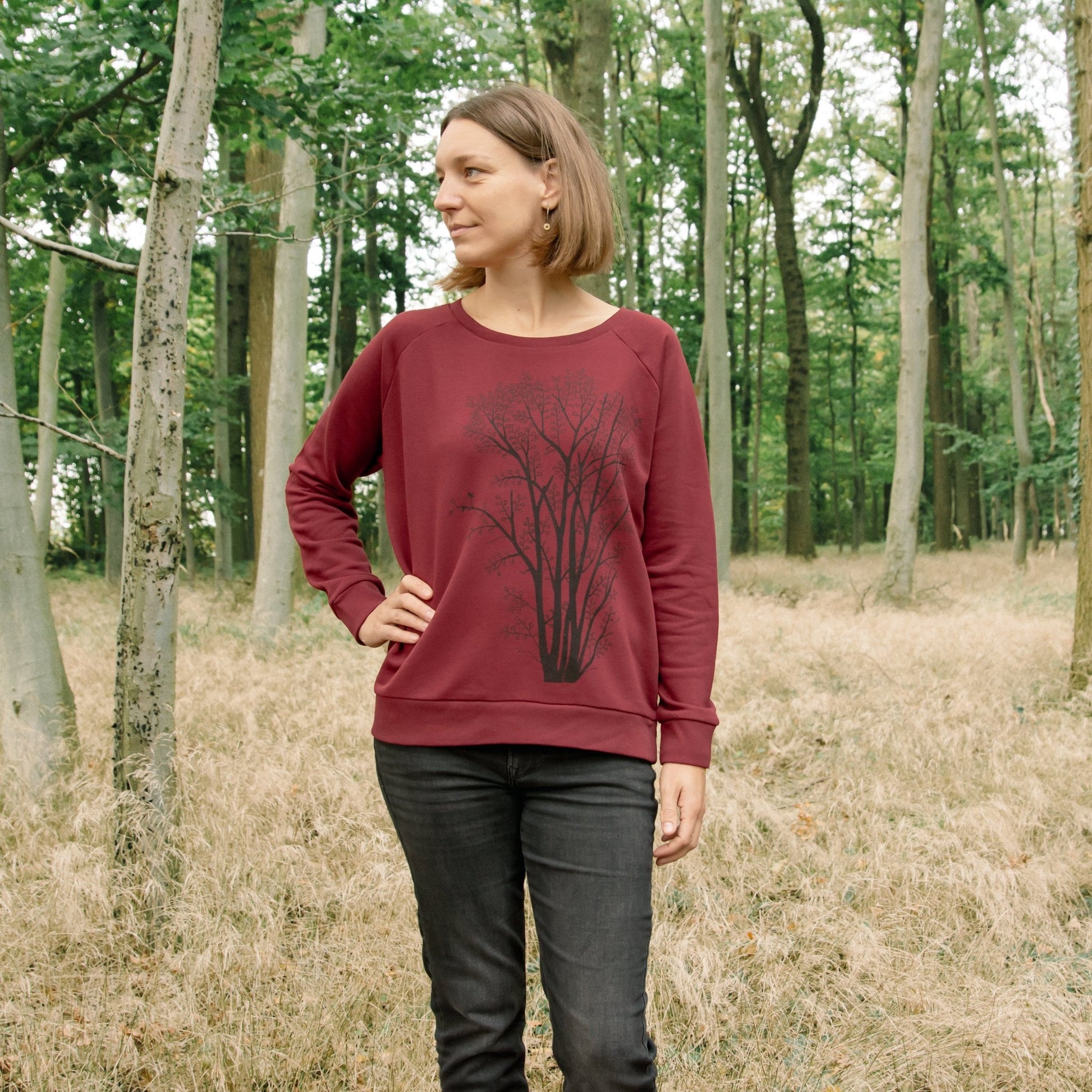 Pullover Baum Kollektion aus nachhaltiger Bio-Baumwolle für Frauen und damen. Eine Frau trägt den weichen, weinroten Kapuzenpulli oder Rundhals-Sweater mit dem gut sichtbaren Pflanzen-Motiv von vorne.
