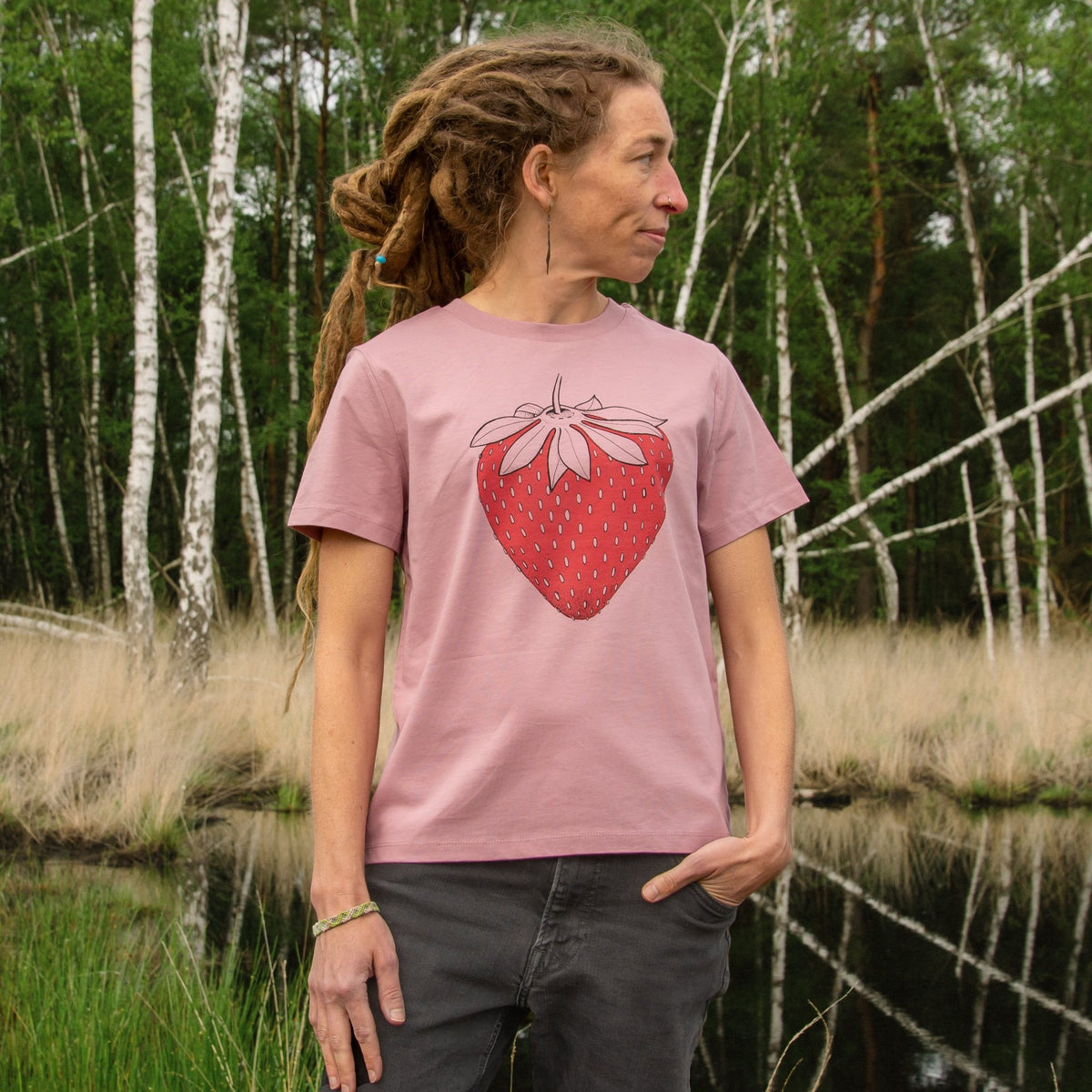 Erdbeer TShirt aus Bio-Baumwolle als nachhaltige Naturmode für Frauen. Eine Frau zeigt das handbedruckte Beeren-Motiv in aufrechter Vorderansicht im Freien.
