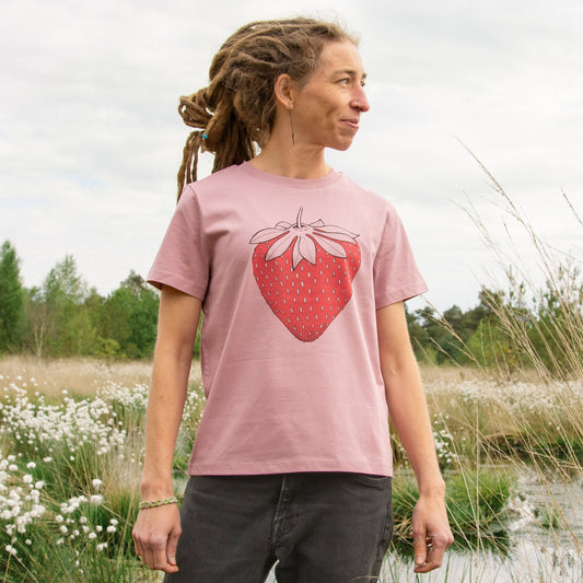 Erdbeer T-Shirt für Damen im lockeren, kurzen Schnitt. Eine Frau steht in der Natur und präsentiert die Vorderansicht des naturfarbenen Bio-Shirts mit der großen Früchte-Illustration.
