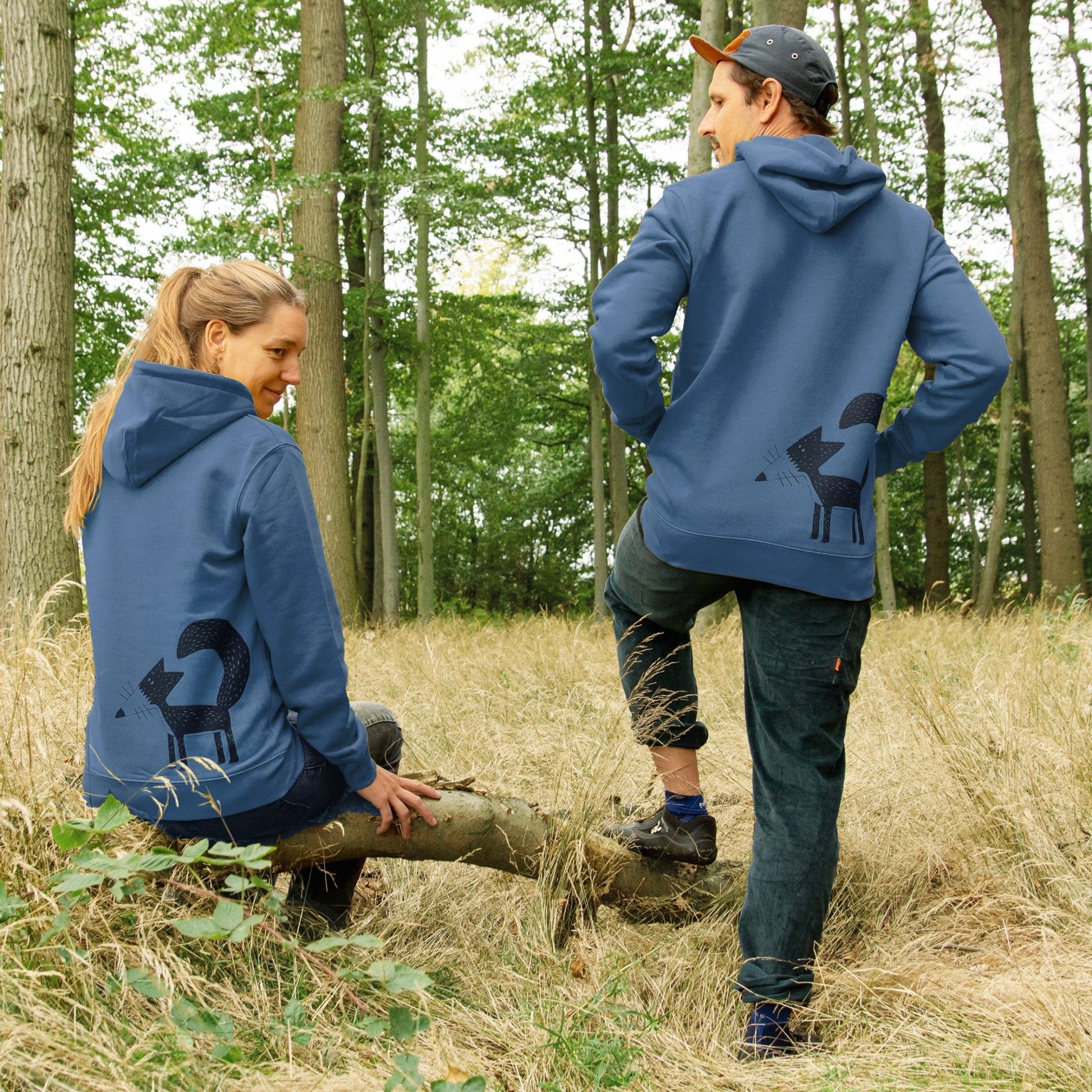 Fuchs Hoodie im Unisex-Schnitt in der Farbe Deep Teal. Eine Frau und ein Mann präsentieren gemeinsam den blau-grünen Partnerlook-Kapuzenpullover mit dem großen Fuchs-Backprint im Wald.
