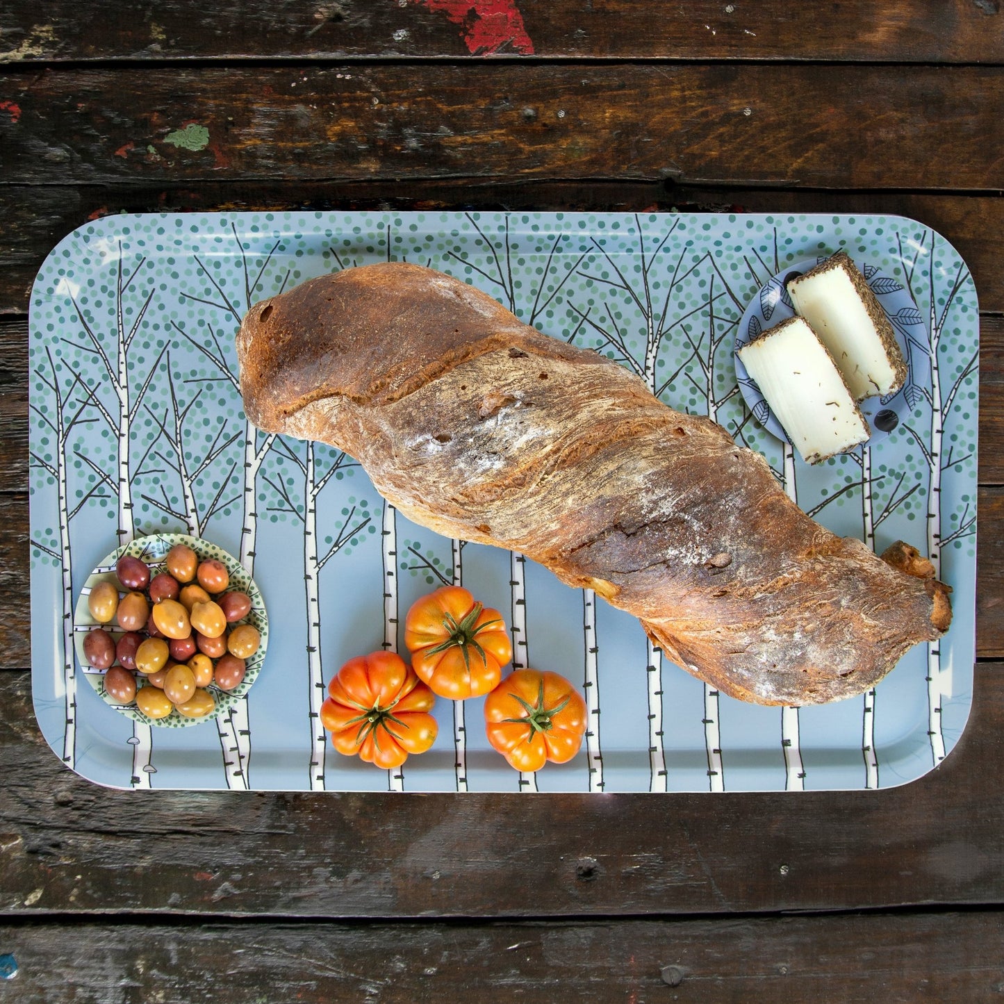 Skandinavisches Frühstückstablett aus Holz mit hellblauem Natur-Design. Großes, rechteckiges Serviertablett (53x32 cm) mit Pflanzen-Muster, belegt mit einem großen Weißbrot und frischen Tomaten für die Küche.