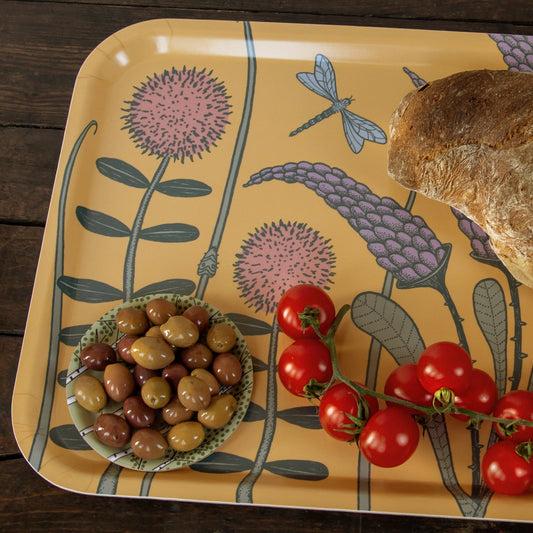 Nahaufnahme von einem bunten Wiesenblumen-Design mit frischen Oliven. Detailansicht des gelben Serviertabletts im Scandi-Style, sommerlich angerichtet mit grünen Oliven und roten Tomaten.