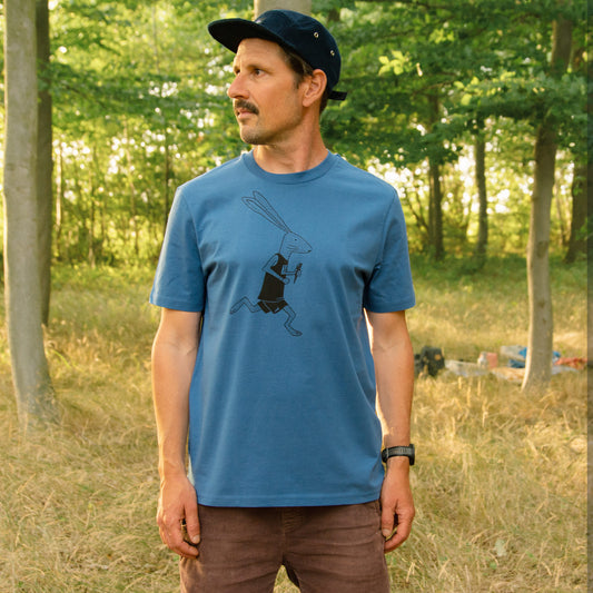 Herren Bio-T-Shirt in Mindful Blue mit großem Laufhasen-Motiv auf der Brust, Model im Wald