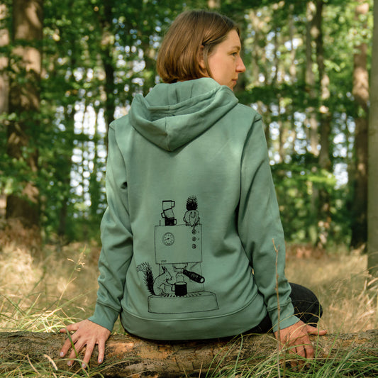Frau sitzt mit Kaffee im Wald und trägt den CMIG Eichhörnchen Kaffee Pullover mit großem Rückseitenmotiv