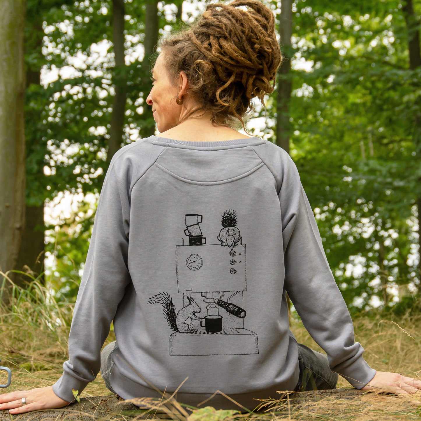 Frau trägt im Wald einen grauen Kaffee Pullover mit Espresso-Motiv und Eichhörnchen auf dem Rückendruck