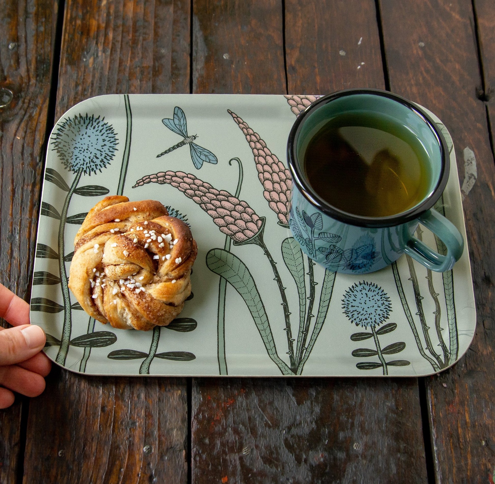Serviertablett im Scandi-Style aus echtem Birkenfurnier in Salbeigrün. Kaffee-Tablett aus schwedischer Produktion, angerichtet mit einer Zimtschnecke und unserer waldgrünen Cmig Emaille-Tasse mit Blaubeer-Motiv für die Kaffeepause.