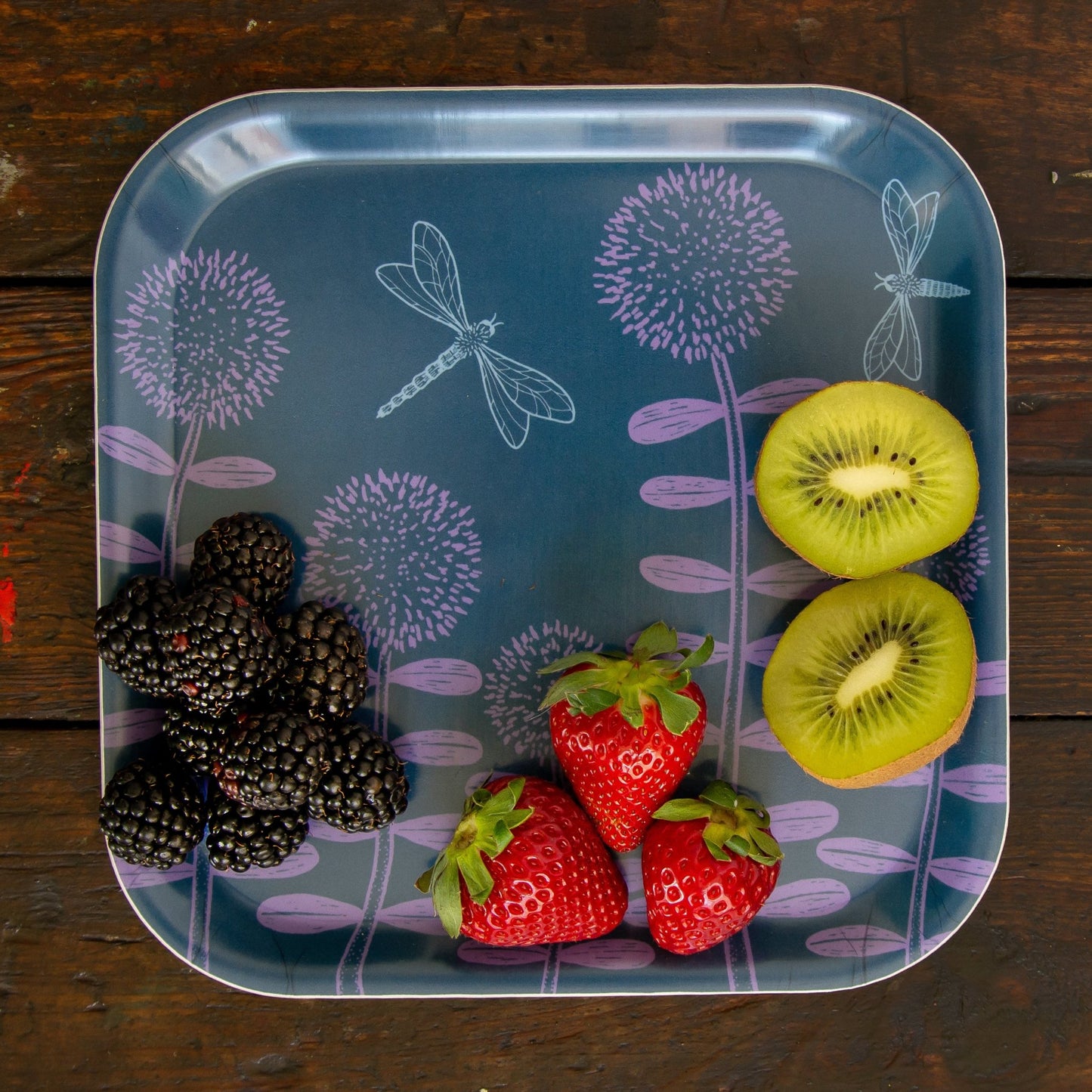 Kleines Frühstückstablett aus Holz im Scandi-Style mit frischem Obst. Quadratischer kleiner Teller mit floralem Muster, wunderschön angerichtet mit geschnittener Kiwi, süßen Erdbeeren und Brombeeren für eine gesunde Pause.