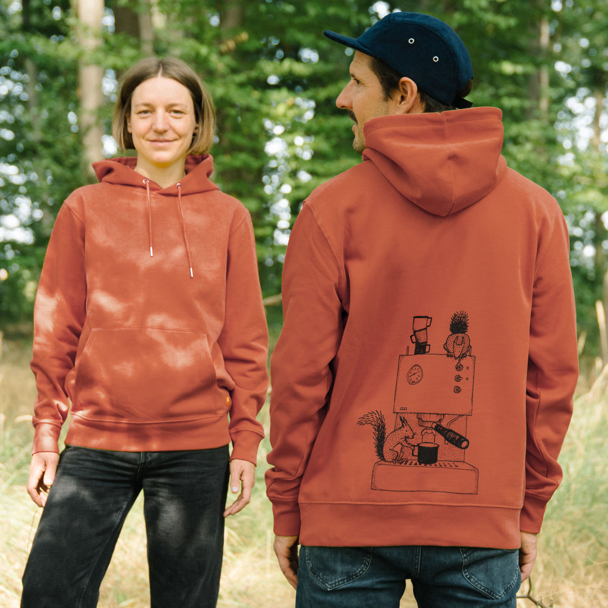 Frau und Mann tragen den CMIG Eichhörnchen Pullover mit Kaffee-Eichhörnchen Motiv beim Spaziergang im Wald