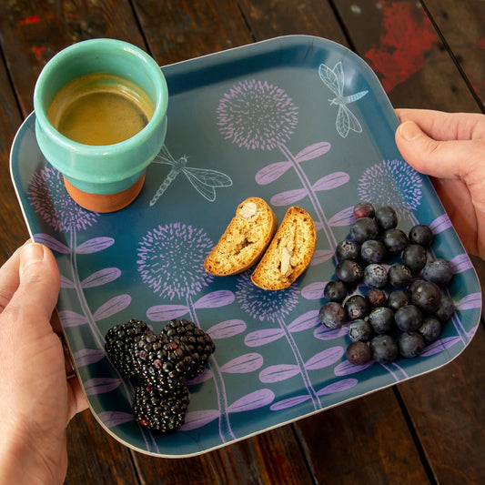 Schwedisches Design Kaffee-Tablett aus Holz mit Espresso und Cantuccini. Kleines quadratisches Serviertablett in Dunkelblau-Lila mit Blumenwiese, sommerlich dekoriert mit einer Espressotasse, italienischem Mandelgebäck, Blaubeeren und Brombeeren.