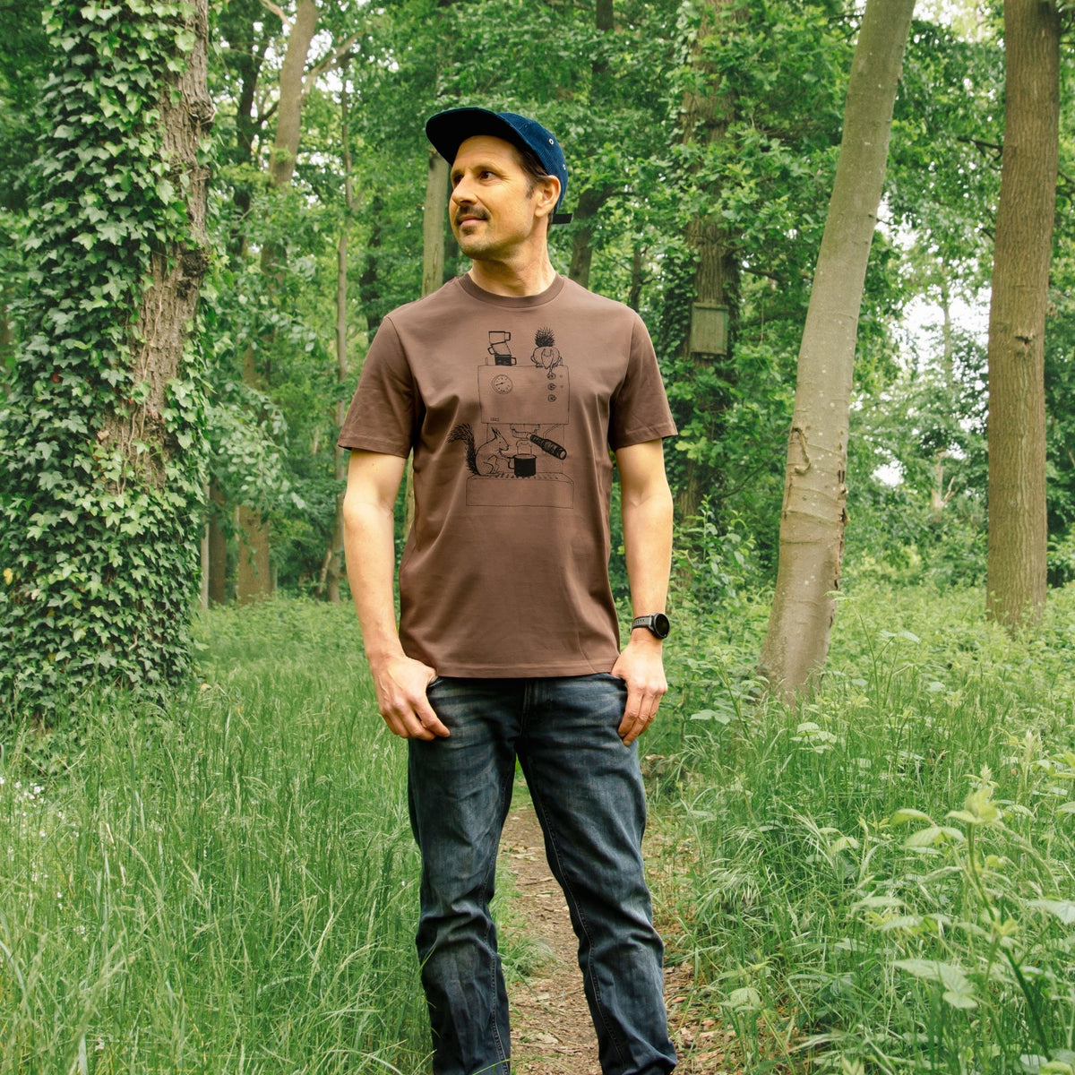 Kaffee T-Shirt für Männer als witzige Geschenkidee für Kaffeeliebhaber. Ein Mann trägt das kaffeebraune Unisex-Shirt aus dem Atelier in Hannover in einer stehenden Outdoor-Pose.