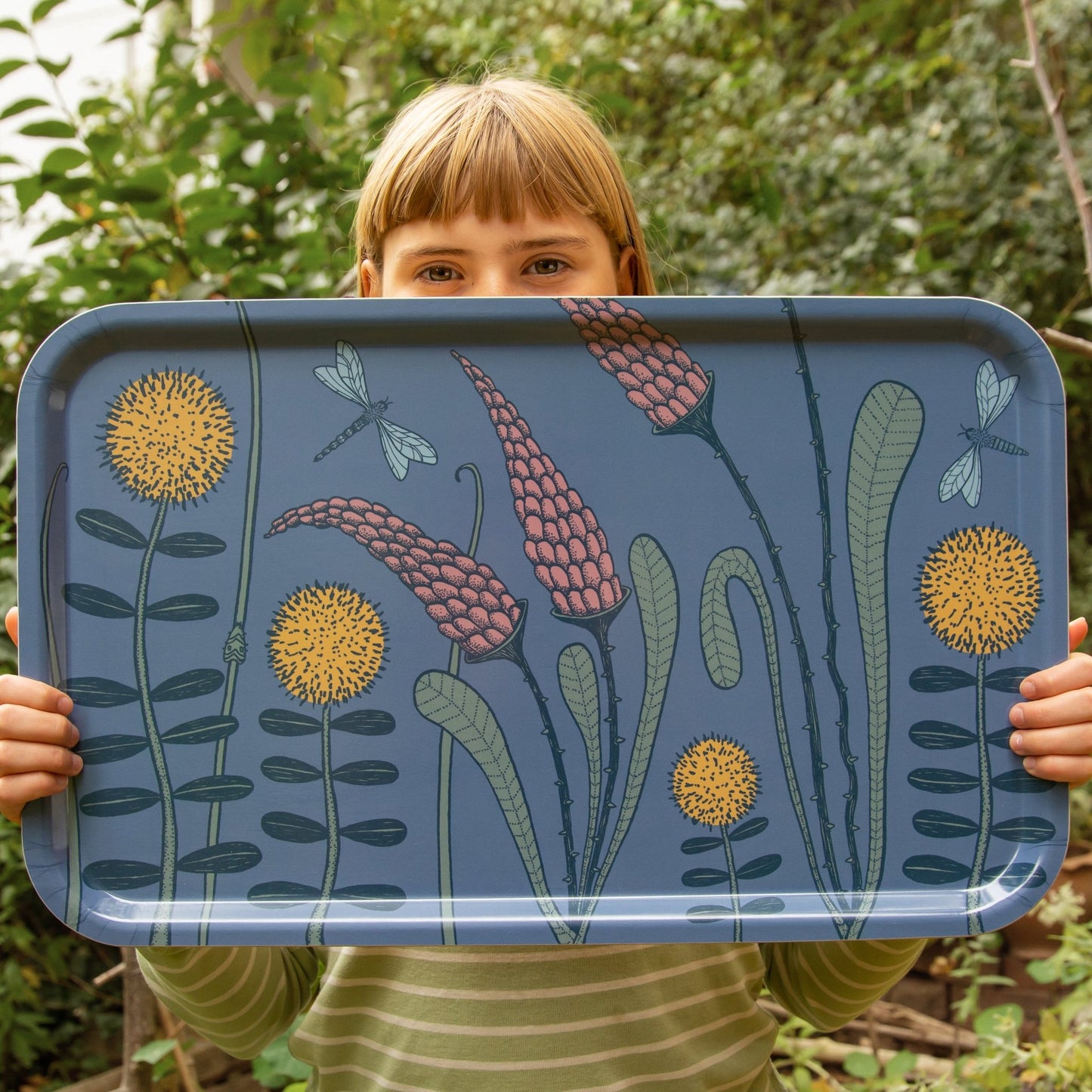 Mädchen hält ein großes skandinavisches Holztablett mit Wiesenblumen-Design. Authentisches Produktfoto unseres deutsch-schwedischen Labels, das sommerliche Gemütlichkeit und florale Kunst zeigt.