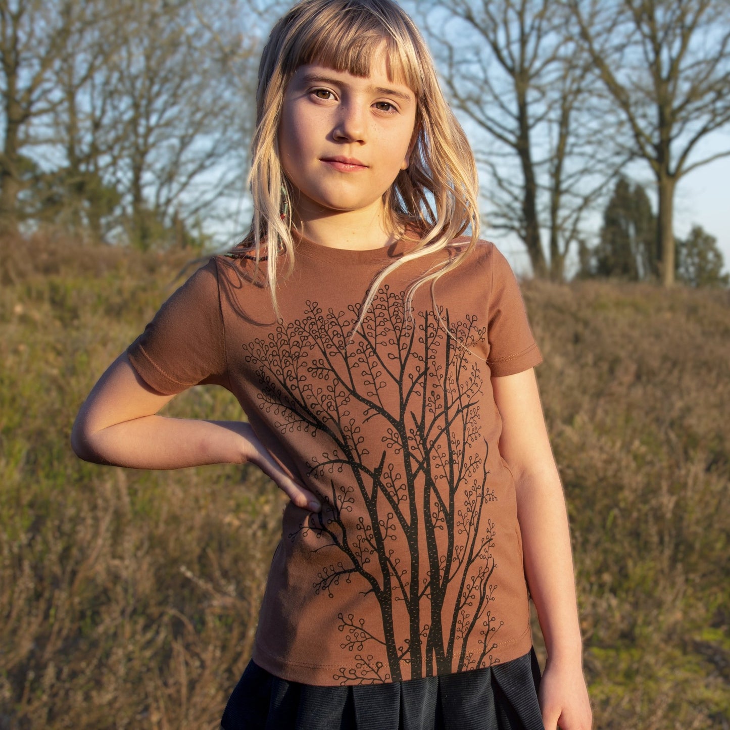 Kinder Tshirt Baum Motiv für Mädchen in der herbstlichen Farbe Braun. Ein kleines Mädchen trägt das handbedruckte Bio-T-Shirt mit dem großen Erlenbaum-Frontprint von vorne.

