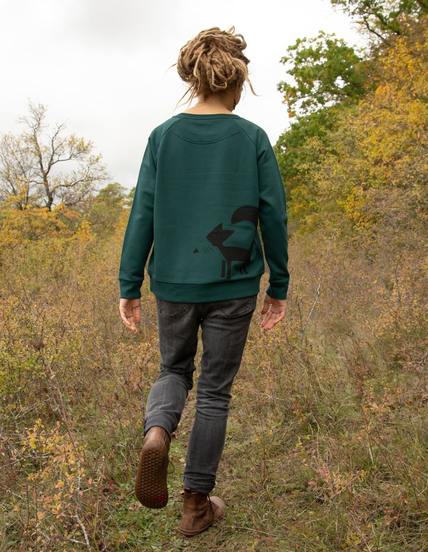 Fuchs Pullover als nachhaltiges Damen Sweatshirt in Glaze Green. Eine Frau steht im Wald und präsentiert das handbedruckte Bio-Oberteil aus dem Atelier in Hannover.
