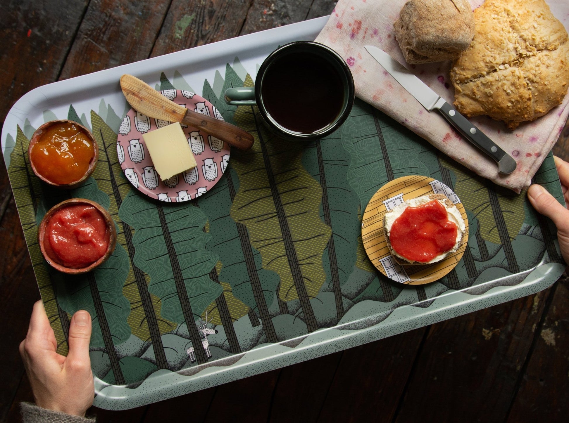Großes Frühstückstablett aus Holz im Scandi-Style reichlich gedeckt. Als Weihnachtsgeschenk gut geignet.Rechteckiges Serviertablett mit Tannenwald- und Rentier-Design, liebevoll angerichtet mit frischem Brot, Butter, Marmelade und einer heißen Tasse Tee für den Morgen.