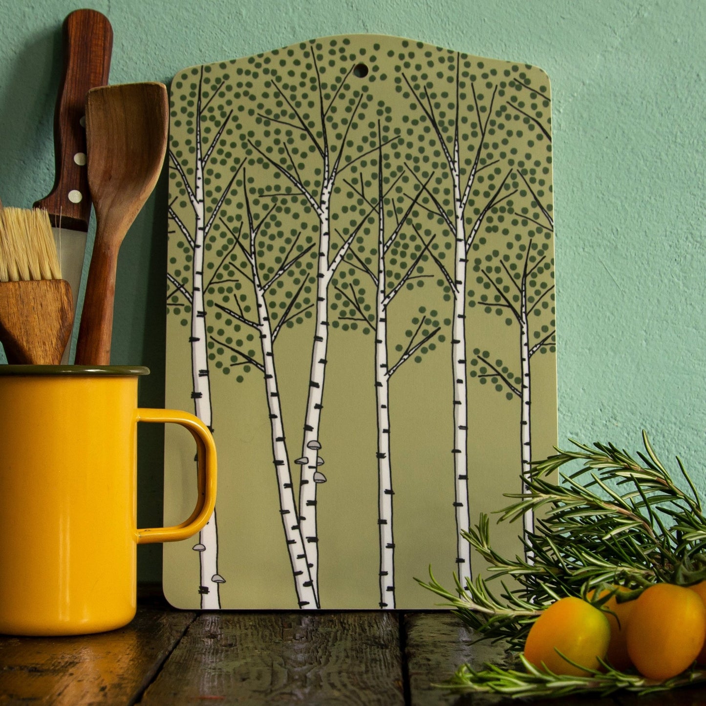 Deko-Brett aus Holz im nordischen Design als Wanddekoration in der Küche. Das grüne Servierbrett mit künstlerischem Birken-Motiv steht dekorativ an der Wand und bringt skandinavische Gemütlichkeit ins Zuhause.